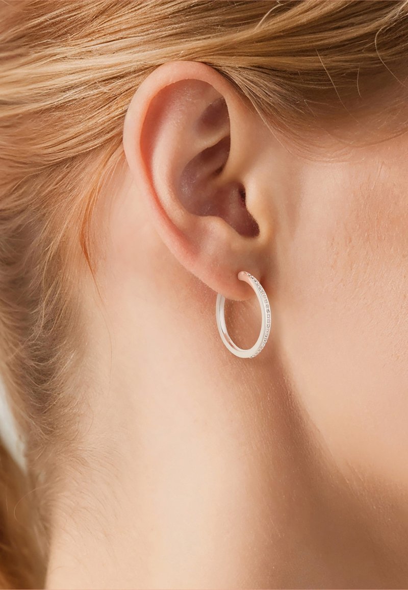 Nahaufnahme eines Ohrs einer Person mit heller Haut und blondem Haar, die einen kleinen, glatten silbernen Creolen-Ohrring trägt.