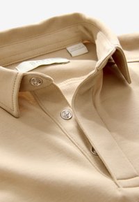 Beige overhemd met kraag, gemaakt van zachte katoen, met een sluiting met zilveren knopen en een label dat aan de binnenkant van de hals is gestikt.