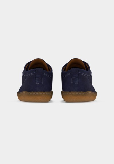 Ζευγάρι παπούτσια από μπλε σουέτ με καφέ λαστιχένιες σόλες, εμφανιζόμενα από πίσω σε λευκό φόντο.