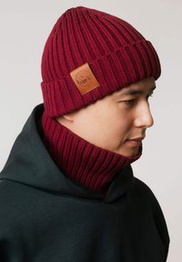Bordowa dzianinowa czapka z prążkowaną fakturą i skórzaną naszywką. W połączeniu z pasującym golfem w ciemnozielonym kolorze.