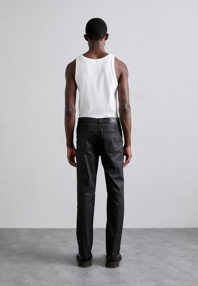 Pantalons noirs à coupe slim, associés à un débardeur blanc sans manches, présentant une texture lisse et un style minimaliste, vus de dos.