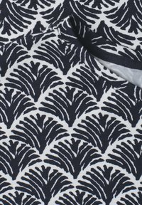 Gros plan d’un tissu noir et blanc avec un motif répétitif en forme d’éventail et des coutures visibles près d’un bord de couture courbé.