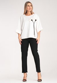 Biała bluzka z krótkim rękawem z czarnym haftem kwiatowym; zestawiona z czarnymi spodniami z wywiniętymi mankietami i czarnymi sandałami na wysokim obcasie.