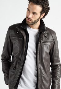 Bruine leren jas met een ritssluiting aan de voorkant, hoge kraag en meerdere zakken; zachte textuur en getailleerde pasvorm; ideaal voor casual gedragen.