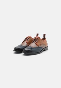Two-tone leather dress shoes featuring a brown upper, black toe cap, intricate brogue detailing, and flat laces with pull tabs on the heel.
