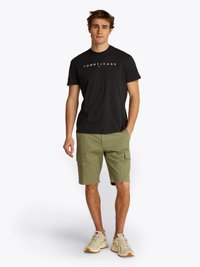 T-shirt en coton noir avec le logo "TOMMY JEANS", associé à un short cargo vert olive. Chaussures : baskets beiges avec textures variées.