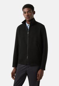 Sort lynlåsjakke med høj krave, sidelommer og ærmer i fuld længde; glat tekstur og minimalistisk design.