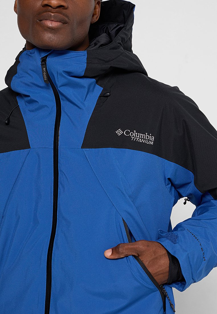 Blaue und schwarze wasserdichte Jacke mit Reißverschluss, verstellbarem Kragen und auffälligem Columbia Titanium-Logo auf der Brust.