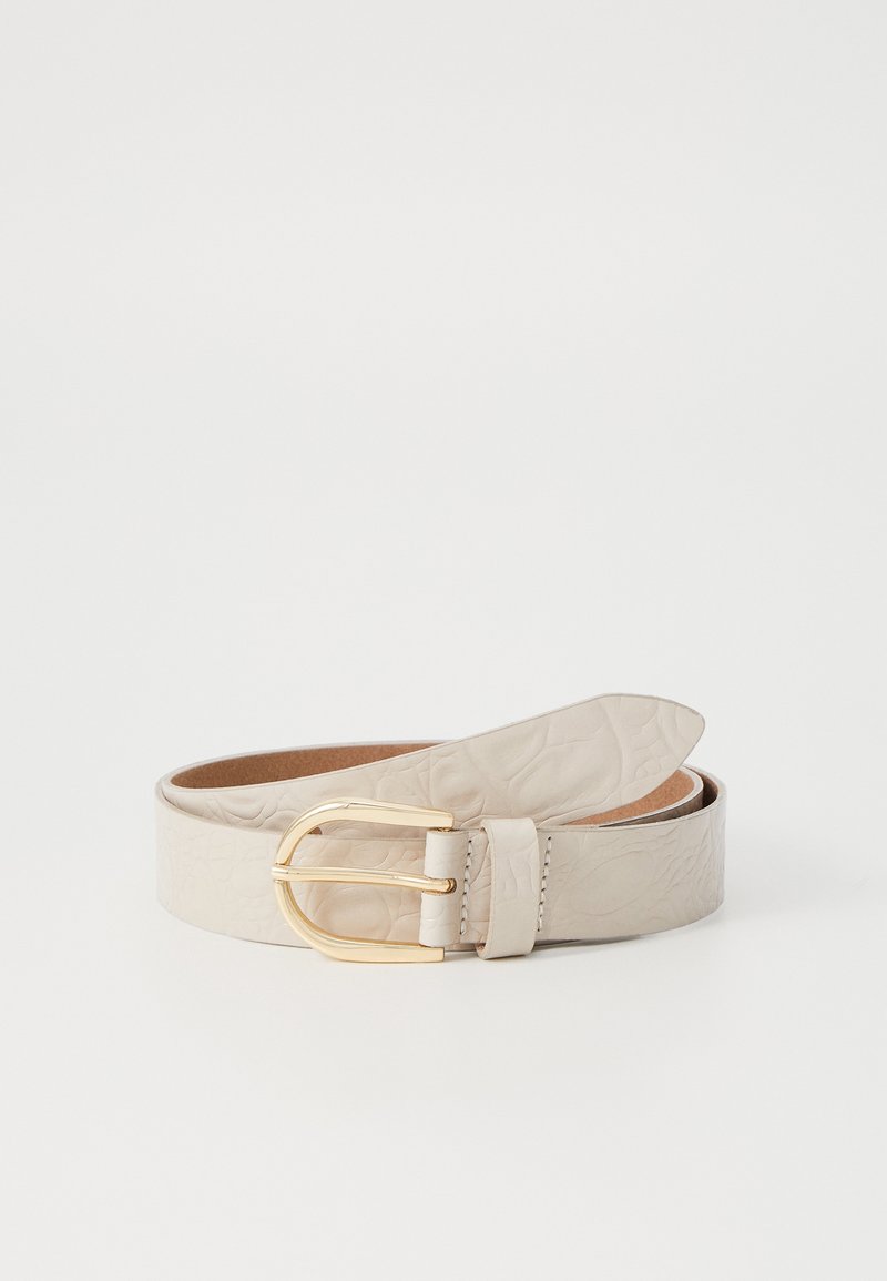 Ceinture en cuir beige clair avec un motif embossé subtil et une boucle dorée arrondie, enroulée sur un fond blanc uni.