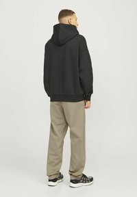 Sudadera con capucha negra hecha de tejido suave, con un corte relajado y puños acanalados. Combinada con pantalones beige claros y zapatillas negras.