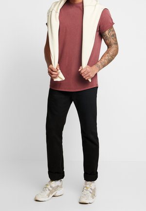 T-shirt bordeaux, à manches courtes ; pull blanc drapé sur les épaules ; pantalon noir ; chaussures de course claires avec des accents jaunes.