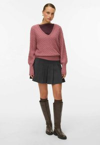 Roosa kabelkootud sviiter V-kaelusega, kombineeritud halli volditud seeliku ja pruunide põlvekõrguste saapatega. Pehme tekstuur ja lõdvik disain.