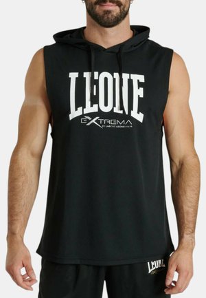Uomo muscoloso che indossa una felpa nera senza maniche e pantaloncini con scritta bianca "LEONE EXTREMA" sul petto e sulla coscia sinistra.
