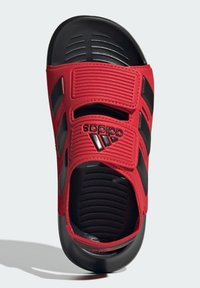 Des sandales rouges à glissière avec des accents noirs, dotées de deux sangles ajustables, d'un pied de resserrement texturé et de trous de ventilation sur les côtés. Logo Adidas affiché.