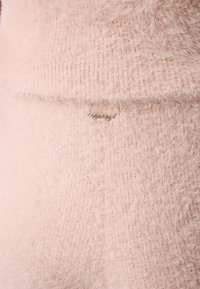 Gaiši rozā adīta džemperis ar pūkainu tekstūru, kuram ir zelta "guess" logo birka. Mīksta materiāla, nedaudz slāņota konstrukcija.