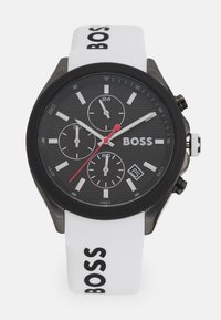 Black dial watch with three sub-dials, red accent, and white silicone strap featuring 'BOSS' logo, black case, and textured finish.
