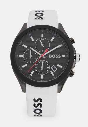 Montre à cadran noir avec trois sous-cadrans, accent rouge et bracelet en silicone blanc arborant le logo 'BOSS', boîtier noir et finition texturée.