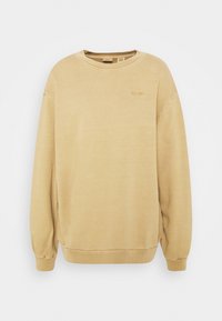 Sweat-shirt beige en coton doux, col rond, épaules tombantes, poignets et ourlet côtelés, avec un petit logo brodé sur la poitrine.