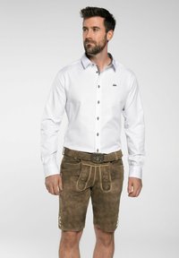 Camisa blanca de manga larga con botones y logo en el pecho, combinada con pantalones cortos de piel marrón con costuras decorativas y botones.