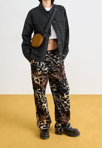 Svart knäppjacka över en vit crop top, matchad med bruna och svarta leopardmönstrade byxor och svarta plattformstövlar. Liten brun axelväska.