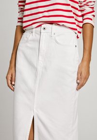 Hvit denim skjørt med splitt foran, høy midje og beltehemper. Har sidelommer og diskrete sømdetaljer. Kombinert med en rødstripet topp.