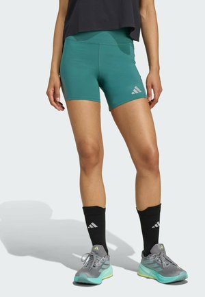 Teal athletic shorts made of stretchy fabric with a smooth texture. Features logo accents and a high waist design. Paired with gray sneakers and black socks.
