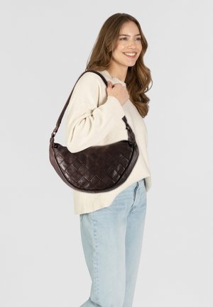 Borsa a tracolla in pelle marrone con un design trapuntato, forma arrotondata e tracolla intrecciata, esposta con un maglione bianco e jeans blu.