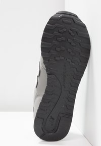 Semelle de chaussure avec bande de roulement en caoutchouc noir présentant des motifs en zigzag et ondulés, texturée pour l’adhérence, fixée à une basket blanche.