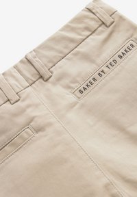 Kaki kokvilnas bikses ar gludu tekstūru, kurām ir redzama etiķete "BAKER BY TED BAKER" un divas aizmugures kabatas.