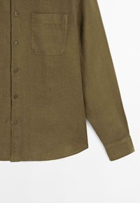 Olive green long-sleeve shirt made of textured fabric, featuring a front chest pocket and round hem with button-up closure.