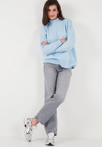 Gaiši zils adīts džemperis ar augstu apkakli, kombinēts ar pelēkiem taisnajiem džinsiem un daudzkrāsainām sporta apaviem. Brīva piegriezuma un teksturēts audums.