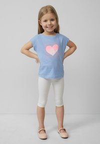 Lichtblauwe t-shirt met een roze hartgrafiek en tekst, gekleed met witte leggings en lichtroze schoenen. Glad, casual stof en pasvorm.
