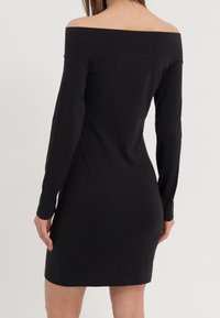 Robe noire, décolletée et sans manches, fabriquée en tissu doux, avec des manches longues et une silhouette ajustée, ornée d'un ourlet droit et sans motifs visibles.