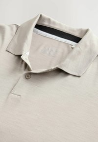 Lys beige polo-shirt med en tekstureret overflade, tre-knaps placket og en sort mesh kraveforing. Har et diskret logo på brystet.