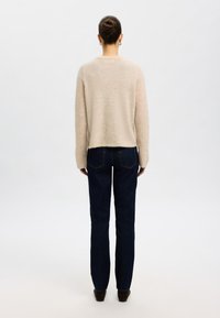 Light beige sweater with a soft texture, crew neck, and long sleeves, paired with dark blue straight-leg jeans and black shoes.