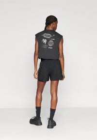 Μαύρο αμάνικο crop top με γραφικά σχέδια, συνδυασμένο με μαύρο σορτς. Το ντύσιμο έχει άνετη εφαρμογή και μαλακή υφή.