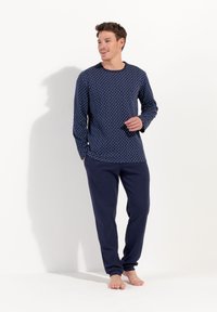 Marineblå langærmet top med geometrisk mønster, parret med marineblå sweatpants. Glat tekstur, afslappet pasform, enkelt design uden detaljer.