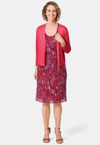Bloemdruk jurk in tinten rood en paars, met een tailleband. Lichtgewicht, gelaagd materiaal en een effen roze cardigan complementeren de look.
