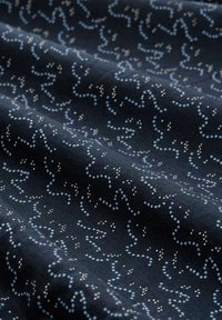 Marineblauer Stoff mit einem wellenförmigen Muster aus hellblauen und weißen Punkten. Die Textur wirkt weich und glatt, geeignet für verschiedene textile Anwendungen.