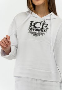 Sudadera blanca con un gráfico negro de "ICE ICEBERG" con acentos florales. Fabricada en tela suave, tiene un bolsillo canguro y cordones.