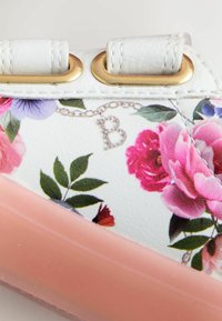 Floru raksta sporta apavs ar baltu mākslīgās ādas augšdaļu ar rozā akcentiem, zelta aculetēm un dekoratīvu ķēdes detaļu ar "B".