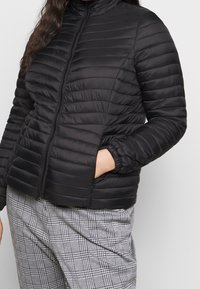 Giacca imbottita nera con collo alto, motivo trapuntato e chiusura frontale con cerniera. Presenta polsini elasticizzati e tasche laterali.