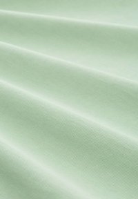 Világos menta zöld textil, amely texturált, szőtt megjelenésű, puha, redős hajtásokkal és finom árnyalat-változásokkal.