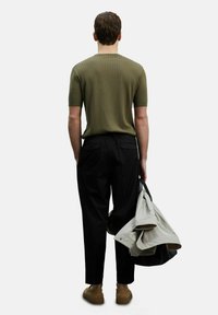 Olijfgroene geribbelde shirt met korte mouwen, zwarte broek en lichtgrijze jas, in één hand gehouden, platte schoenen, eenvoudig ontwerp, neutrale kleuren.