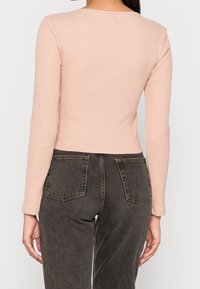 Dlouhý rukáv, přiléhavý top ze světle růžového žebrovaného materiálu, spárovaný s tmavě šedými džíny s vysokým pasem, které mají zadní kapsy a jemný omak.