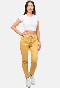 Pantalon en coton jaune avec taille à cordon et détail de bouton, associé à un crop top blanc ajusté et des baskets blanches. Texture lisse.