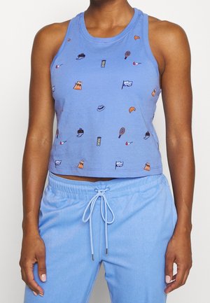 Frau trägt ein hellblaues ärmelloses Crop-Top mit kleinen bunten Symbolen und passende hellblaue Jogginghosen mit Kordelzug.