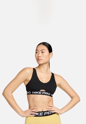 Top sportivo nero con scollatura a barca, dettaglio a taglio e ampia fascia elastica con branding bianco "NIKE PRO". Tessuto morbido e elastico.