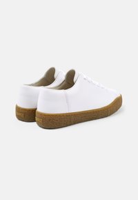 Sneaker in pelle bianca con suola in gomma testurizzata e dettagli di cucitura sottili. Forma arrotondata, design con lacci e stile minimalista.