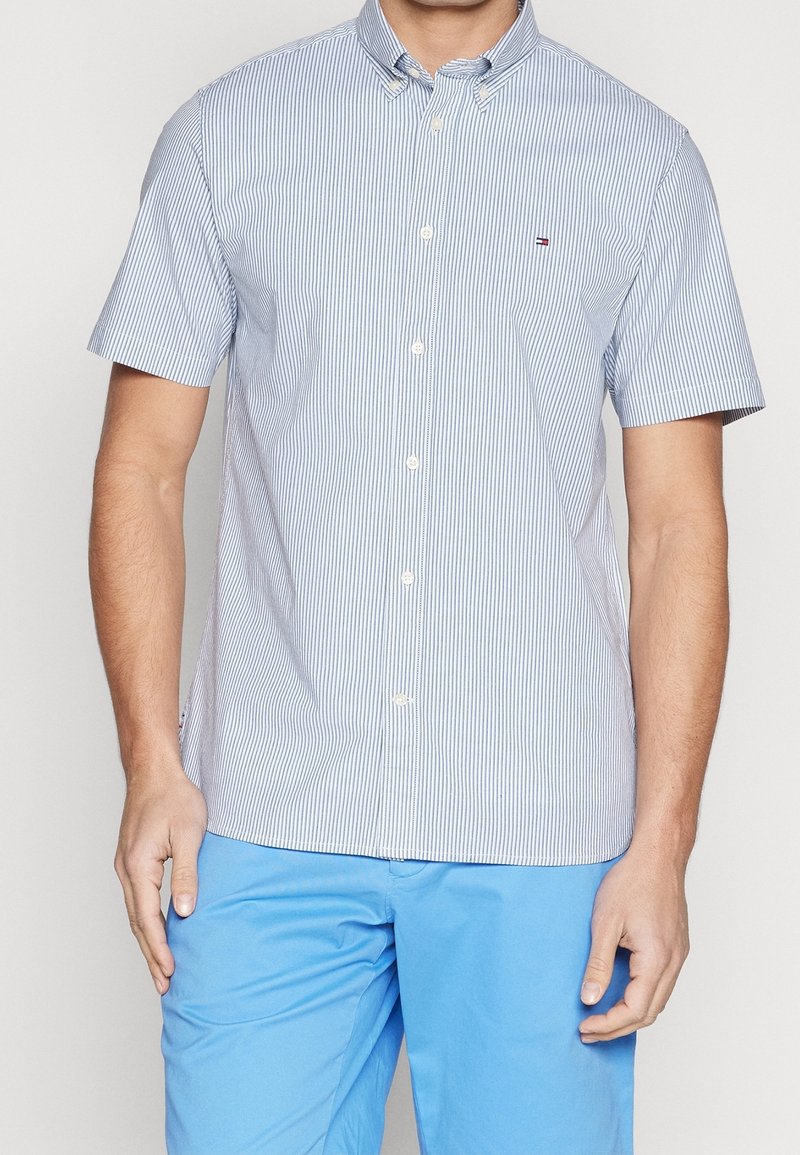 Camicia a maniche corte con bottoni, a strisce blu chiaro e bianche, dettagli del colletto, tasca con logo, abbinata a pantaloni corti blu chiaro.